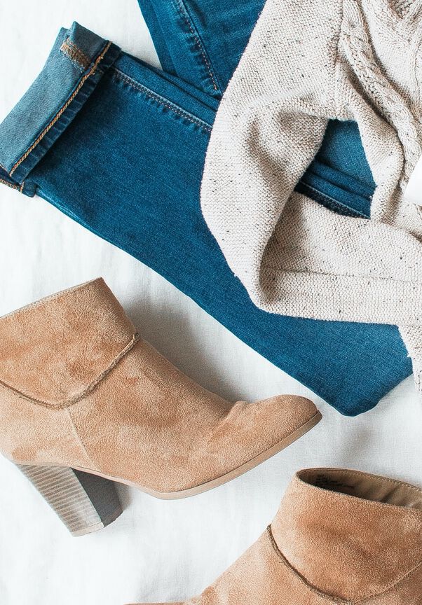 Brown boots, blue jeans and knitwear lying on white ground.