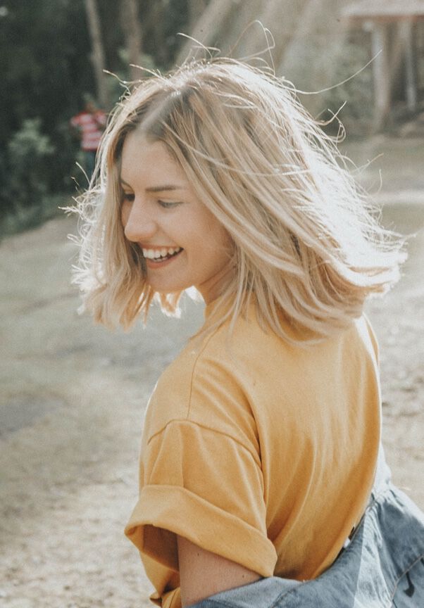 Woman in mustard t-shirt smiling under the lights of a sun.